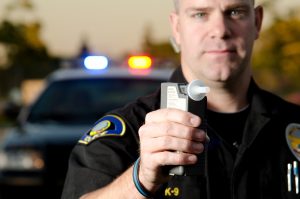 A police officer holding a breath test machine with his police car in the background
